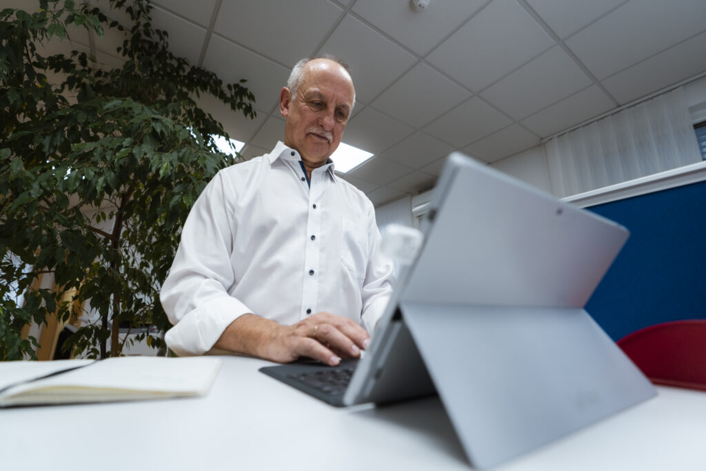 Ein Mann steht vor einem Laptop und arbeitet.